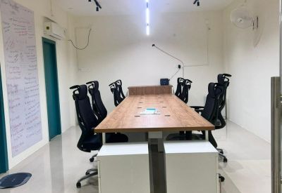 Long wooden communal table with black ergonomic chairs and bright track lighting.