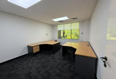 Private office space with two L-shaped wooden desks and dark grey carpeting.