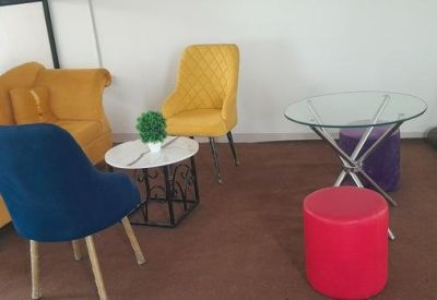 Lounge area with a yellow velvet armchair, a blue chair, and small coffee tables.