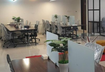 Bright office workspace with multiple rows of wooden desks, white privacy dividers, and modern lighting.