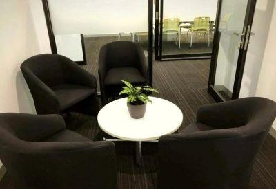 Communal breakout area with black tub chairs surrounding a round white coffee table with a plant.