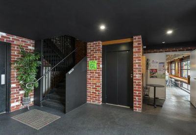 Modern lobby area with exposed brick walls, a staircase, and a black elevator door.
