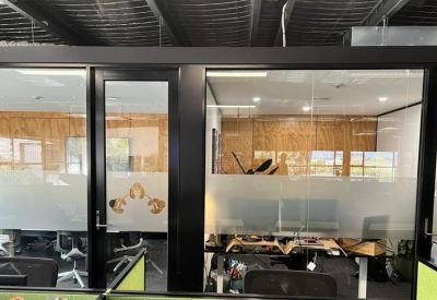 Office workspace viewed through glass partitions with wooden wall accents and black frames.