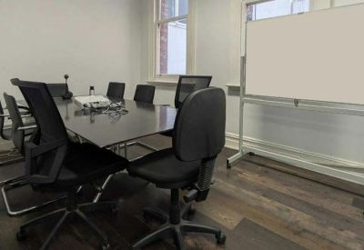 Professional meeting room with a dark boardroom table, black ergonomic chairs, and a mobile whiteboard.