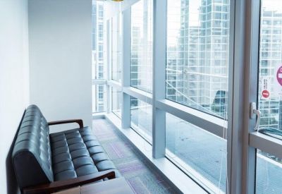 Bright sunlit breakout area with a black tufted leather bench and city views.