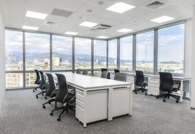 Open-plan office with white workstations and black ergonomic chairs surrounded by floor-to-ceiling windows.