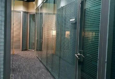 Bright office hallway with glass walls and dark patterned carpet.