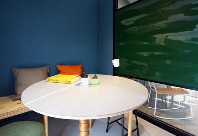 Small meeting corner with a round white table, blue accent wall, and a green chalkboard.