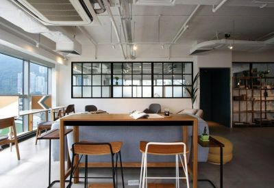 Open-plan coworking area with a high wooden table, stools, and industrial ceiling details.