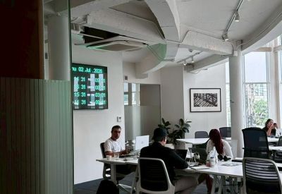 Bright open-plan office with white desks and exposed ceiling pipes.