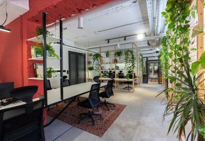 Modern coworking area with long desks, potted plants, and a vibrant red accent wall.