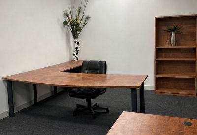 Spacious office suite with a large L-shaped wooden desk and a decorative tall vase.