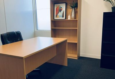 Minimalist office space with a light wood desk, matching bookshelf, and dark carpeting.