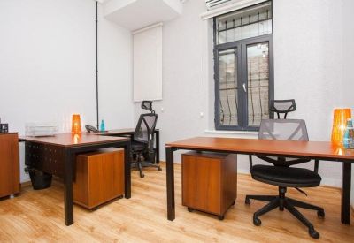 Bright workstation area with two desks, ergonomic chairs, and large windows.