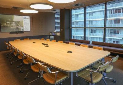 Spacious boardroom with a large light wood table, leather chairs, and city window views.