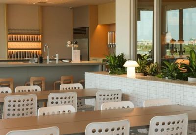 Bright breakout space featuring a kitchen bar and dining tables with white perforated chairs.