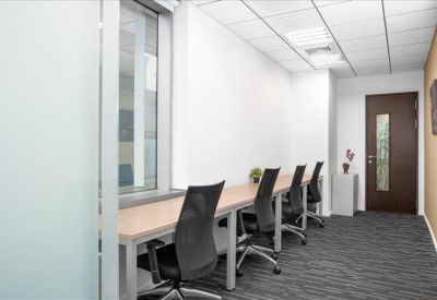 Long workstation desk against a white wall with several ergonomic black mesh chairs.