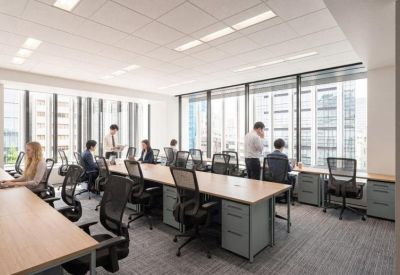 Bright open-plan workspace with long wooden desks and ergonomic chairs near windows.