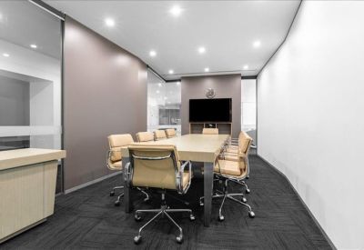 Professional boardroom with a long tan table, matching leather chairs, and wall-mounted screen.