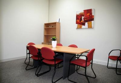 Professional meeting room with a wooden table, red chairs, and modern wall art.