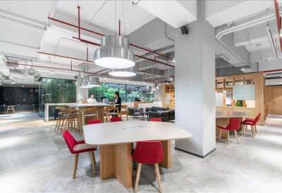 Spacious coworking area with a large central table, red chairs, and industrial ceiling details.