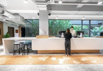 A long, minimalist white reception desk and bar area backed by large windows showing greenery.