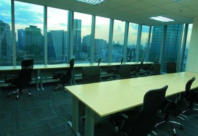 Open-plan workspace featuring wooden desks and black ergonomic chairs against large windows.