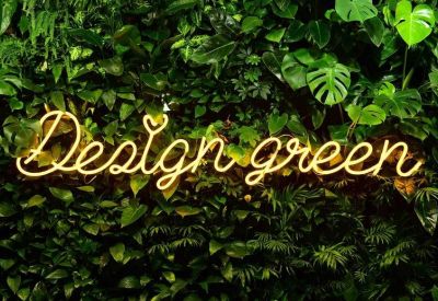 Neon sign reading Design Green set against a lush wall of tropical plants.