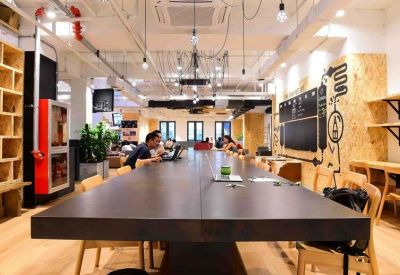 Long dark communal table in a bright open-plan space with warm wood accents and industrial lighting.