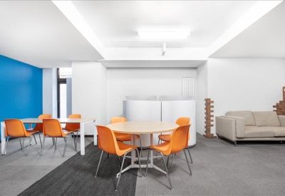 Spacious communal lounge featuring orange chairs, a blue feature wall, and a comfortable beige sofa.