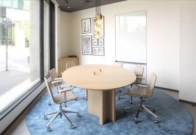 Small meeting room with a round light wood table and blue circular rug.