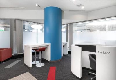 Modern communal area with a bold blue pillar, white high tables, and a curved semi-private pod.