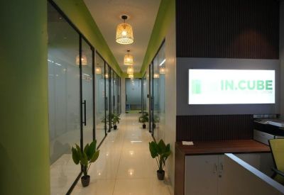Brightly lit hallway with glass-walled offices, potted plants, and warm pendant lighting.
