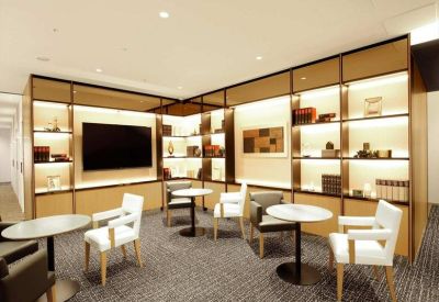 Bright communal lounge with small round tables, white chairs, and illuminated display shelving.