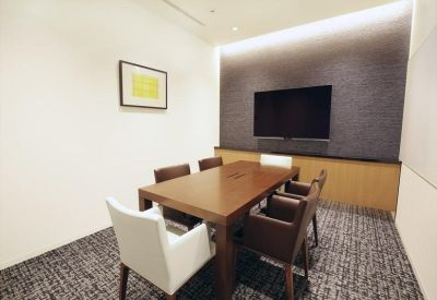 Private meeting room featuring a wooden table, dark chairs, and a wall-mounted screen.