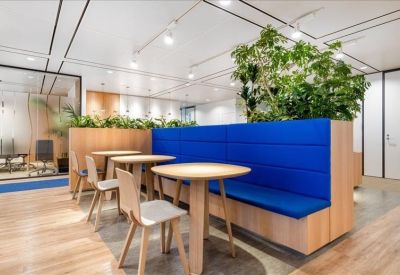 Communal breakout area with small round tables, wooden chairs, and blue bench seating.