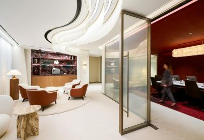 Modern lounge area featuring curved ceiling lights, plush armchairs, and a glass-walled meeting room.