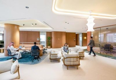 Bright open-plan coworking space with comfortable sofas, wooden pillars, and glass partitions.