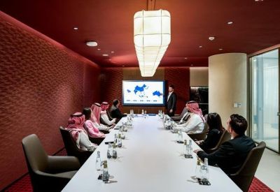Sleek boardroom with a long white table, red textured walls, and a large presentation screen.