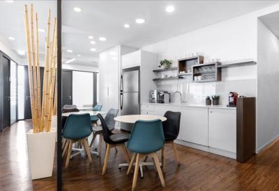 Sleek office kitchen and dining area with teal chairs and wooden flooring.