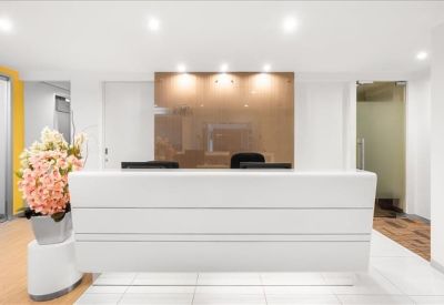 Minimalist white reception desk with a warm wood-paneled feature wall and floral arrangement.