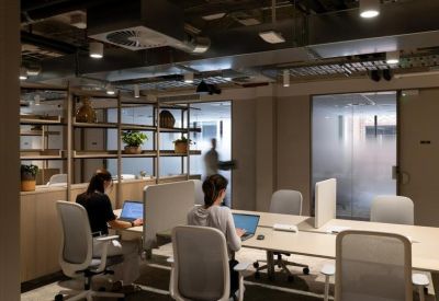Industrial-style workspace with modern desks, ergonomic chairs, and exposed ceiling ductwork.