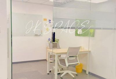 Small internal office suite viewed through a glass partition with a desk and ergonomic chair.