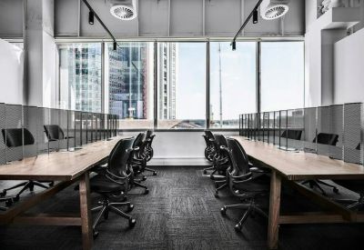 Open-plan office desks with ergonomic chairs facing large windows with city views.