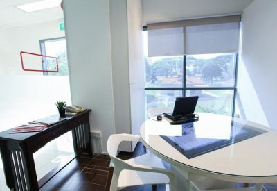Private office suite with a circular white desk, laptop, and large window overlooking greenery.