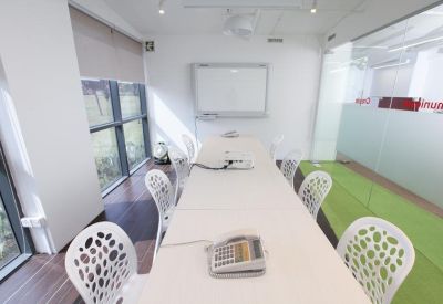 Bright conference room with a long white table, designer white chairs, and a mounted whiteboard.