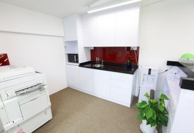 Modern office pantry featuring white cabinetry, a black countertop, and a bold red backsplash.