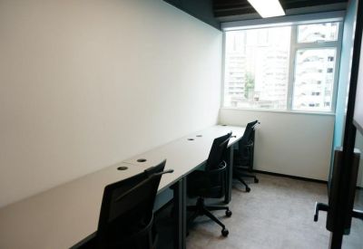 Compact three-person office room with white desks and natural light from a window.