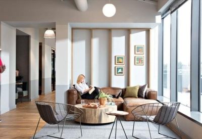 Bright break-out area with a leather sofa, wire chairs, and large floor-to-ceiling windows.