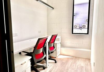 Private office room with two workstations featuring red mesh chairs and white desks.